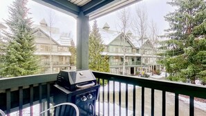 Un balcon doté d’un barbecue, donnant sur un quartier résidentiel avec des maisons et des arbres.