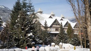 Un grand bâtiment à plusieurs étages, dont le toit est recouvert de neige et qui possède de nombreuses cheminées, entouré d’arbres chargés de neige.