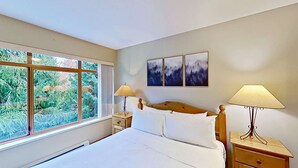 A bedroom with a large window, a bed, two bedside tables with lamps, and three framed pictures on the wall. - Whistler - Northstar 93 (Whistler)