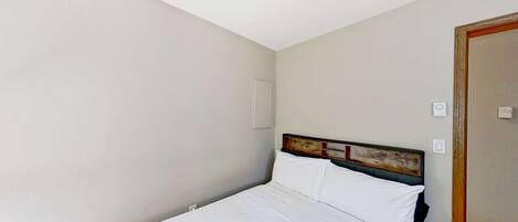 A single bed with white bedding in a room with plain walls and a wooden headboard.