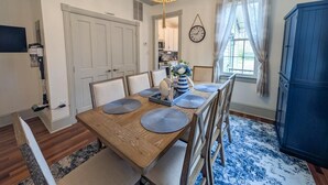 Een eetruimte met een houten tafel, stoelen, een kroonluchter, een klok en een blauwe kast.