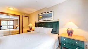 Ein Hotelzimmer mit Bett, Nachttischlampen, einem Nachttisch, einem Spiegel und einem Gemälde an der Wand.