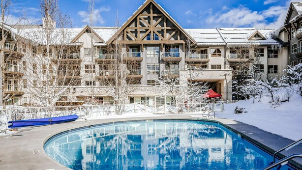 Ett hotell med en pool, snötäckta träd och en skidstuga i bakgrunden.