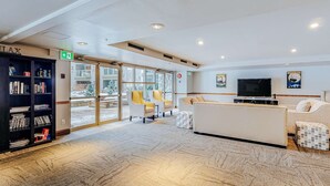 En rymlig entréhall med ett stort bokskåp, en sittgrupp med soffa och fåtöljer, en tv och ett stort fönster med utsikt över omgivningen.