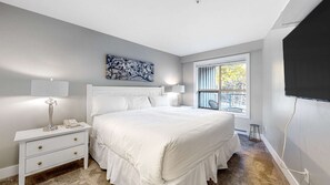 A bedroom with a large bed, bedside lamps, a telephone, a nightstand, a painting, a window, and a TV. - Whistler - The Aspens 233 (Whistler)