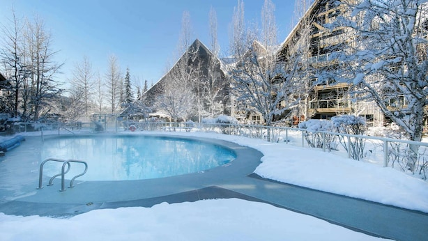 A snow-covered outdoor pool area with a clear sky, surrounded by buildings and bare trees. - Whistler - The Aspens 263 (Whistler)