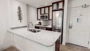 Une cuisine de taille réduite, dotée d’un plan de travail en granit, d’appareils électroménagers en acier inoxydable et de meubles de rangement en bois foncé.