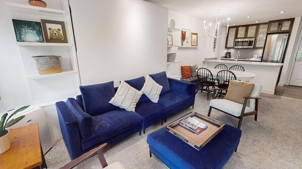 Una sala de estar moderna con un sofá azul, una mesa de centro y un comedor con una mesa y sillas blancas.