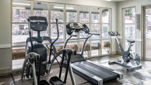 Un gimnasio con cintas de correr, elíptica y bicicleta estática, amplias ventanas con vista a un paisaje nevado.