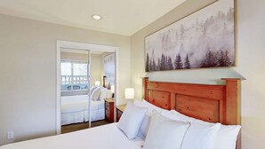 Une chambre d’hôtel avec un lit, une table de chevet, un tableau représentant une forêt et une vue sur l’extérieur, visible à travers une porte.