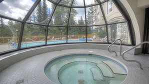 Ein Hallenbad mit Glasdecke, umgeben von Fliesenboden und einer Steinwand.