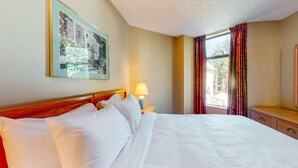 Ein Hotelzimmer mit einem großen Bett, einem Nachttisch mit Lampe, einem gerahmten Bild an der Wand und einem Fenster mit Vorhängen.