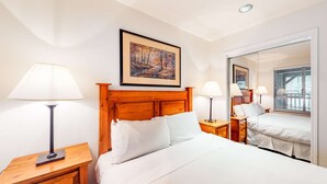 Ein Hotelzimmer mit Holz-Kopfteil, einem großen Bett mit weißer Bettwäsche, zwei Nachttischen mit Lampen, einem gerahmten Gemälde über dem Bett und einem großen Spiegel, der den Raum reflektiert.