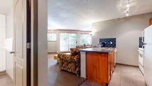 Una cocina moderna con una isla integrada, un comedor con un sofá estampado y grandes ventanales que ofrecen luz natural.