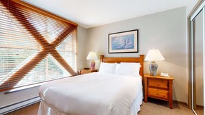 Una habitación de hotel con una cama grande, cabecera de madera, dos mesitas de noche con lámparas y un cuadro en la pared.