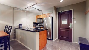 A compact kitchen with a central island, stainless steel appliances, and a dark wooden door. - Whistler - Town Plaza 302 (Whistler)