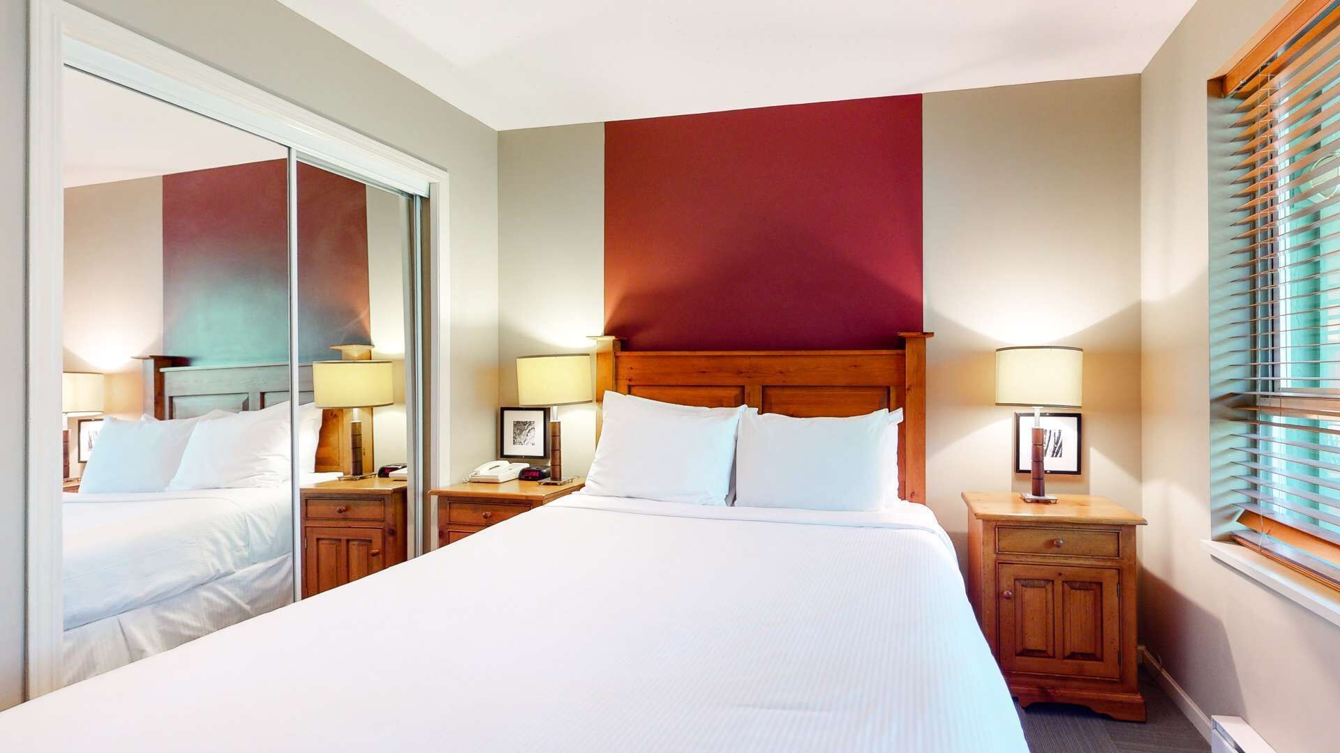 Een hotelkamer met een groot bed, twee nachtkastjes met lampen, een houten hoofdbord en een grote spiegel.