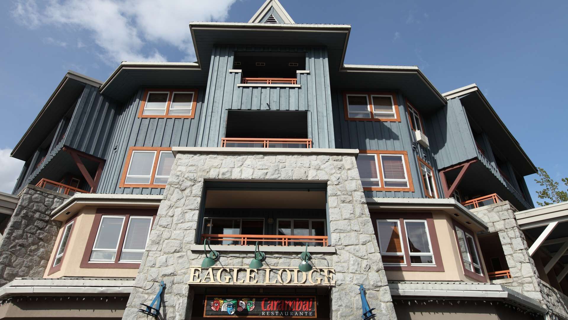 Un immeuble à plusieurs étages avec une façade en pierre, de grandes fenêtres et une enseigne indiquant « Eagle Lodge Caramba Restaurante ».