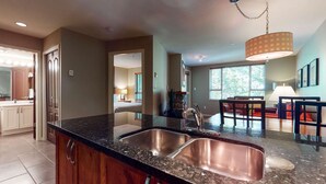 A modern kitchen with a double sink, granite countertops, and a dining area with a table and chairs. - Whistler - Town Plaza 302 (Whistler)