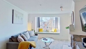 Un soggiorno con divano, tavolino, televisore e finestra vista alberi.