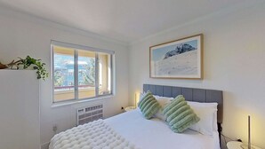 Una camera da letto con un letto, una finestra, un termosifone, un quadro appeso al muro e una pianta.
