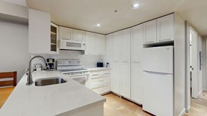 Una cocina moderna con armarios blancos, un lavamanos de acero inoxidable, un microondas integrado y un refrigerador.