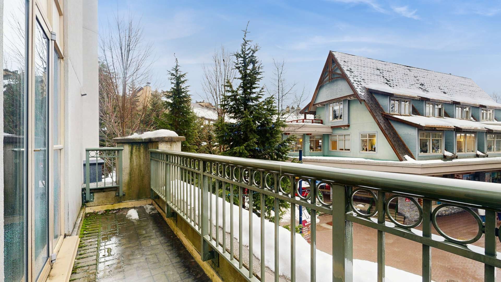 Un balcon avec une balustrade en métal, un escalier et une vue sur un immeuble doté de nombreuses fenêtres et d’un toit enneigé.