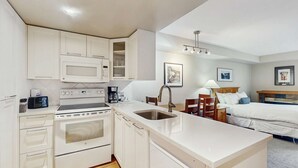 Una habitación de hotel pequeña con kitchenette, una cama, una mesita de noche y una lámpara.
