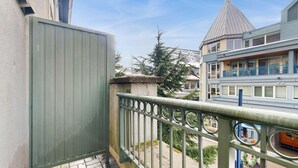 Un balcón con baranda metálica, una reja verde y vista a un edificio de techo cónico.