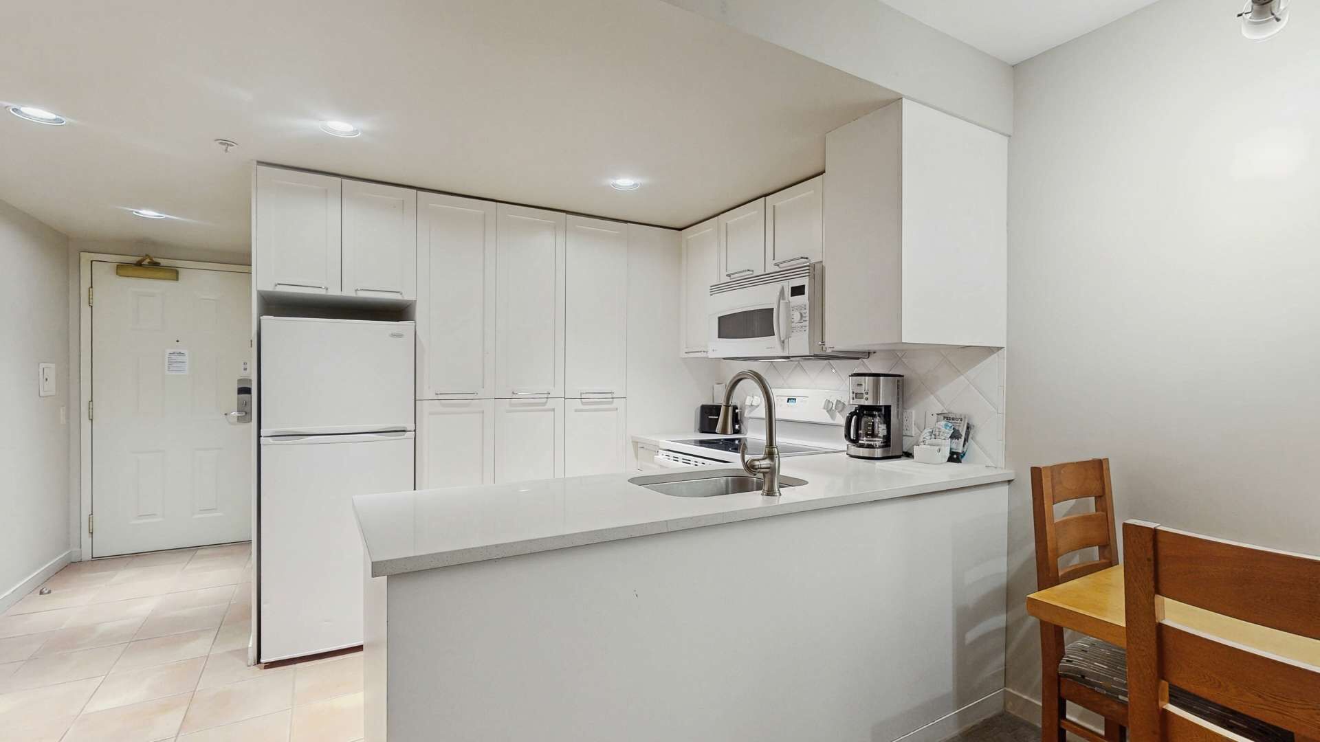 Una cocina moderna con armarios blancos, microondas integrado, cafetera y lavamanos.