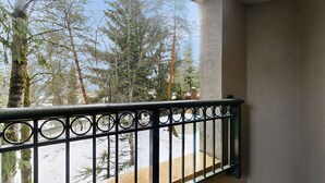 Ein Balkon mit Metallgeländer, der auf eine verschneite Landschaft mit Bäumen blickt.