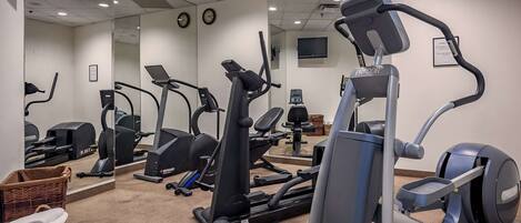A gym with various cardio machines, a mirrored wall, and a clock.