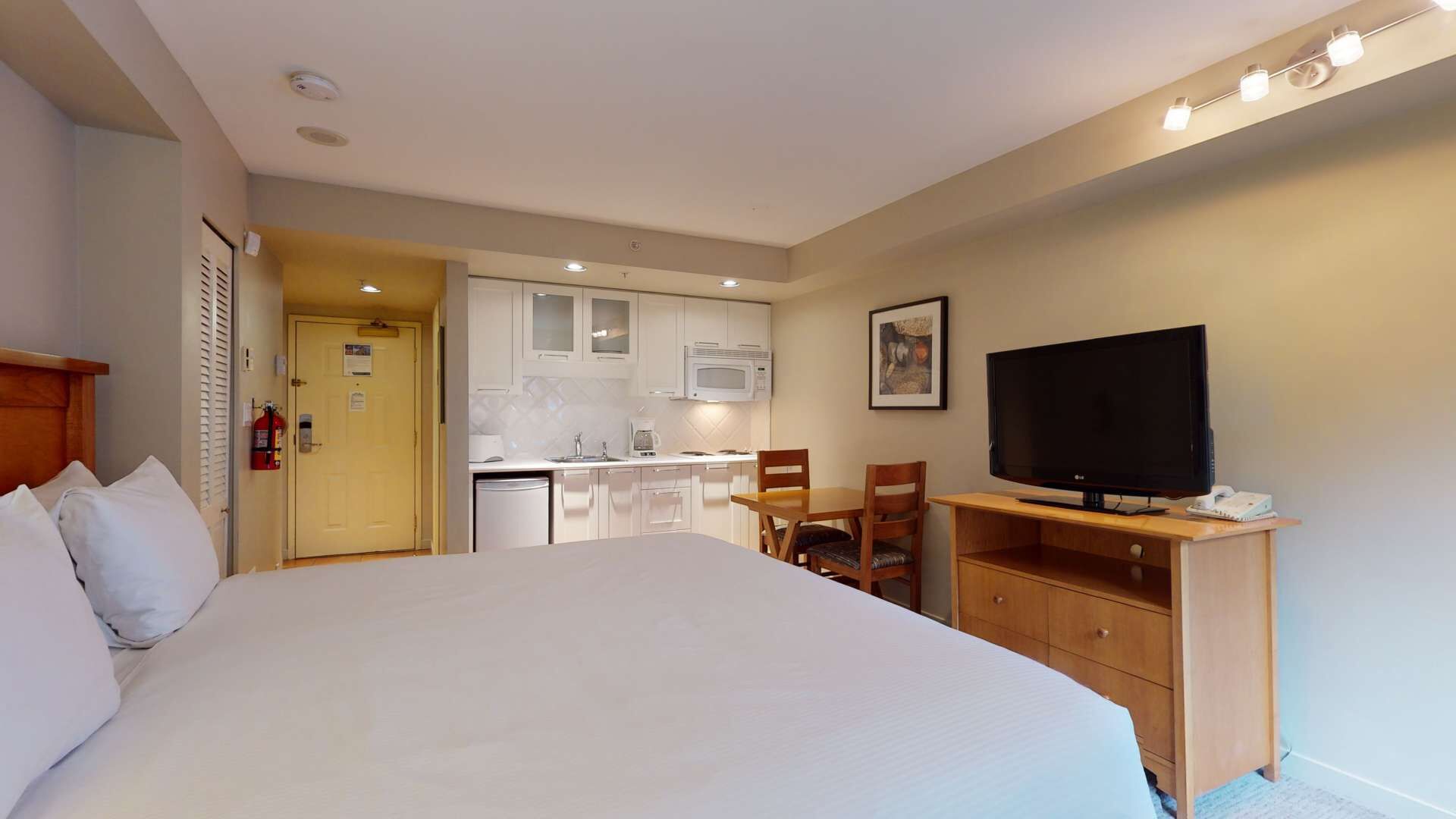 Une chambre d’hôtel comprenant un grand lit, une télévision, un bureau avec une chaise, une kitchenette et une salle de bain.