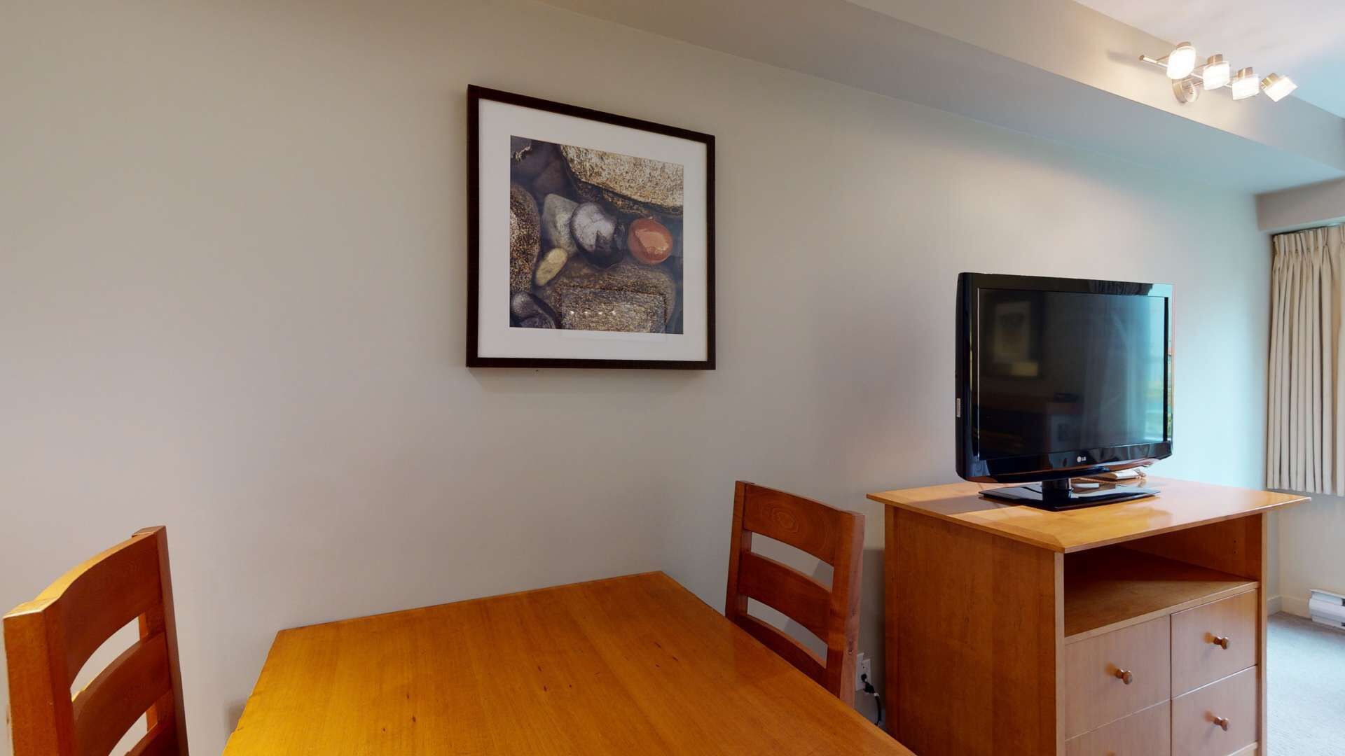 Una habitación con una mesa de madera, dos sillas, un cuadro en la pared y un televisor sobre un mueble de madera.