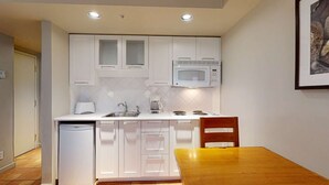 Una cocina compacta con armarios blancos, microondas, cafetera y lavamanos.
