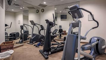 Un gimnasio con máquinas de cardio, un espejo grande y un reloj.