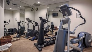 Ett gym med olika konditionsträningsmaskiner, en vägg med speglar och en klocka.