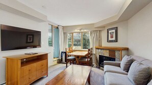Ein Wohnzimmer mit Flachbildfernseher, Holz-Entertainment-Möbel, Esstisch mit Stühlen und einer Couch.