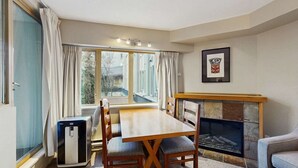 Ein Zimmer mit Esstisch, Stühlen, Kamin und einem großen Fenster mit Vorhängen.