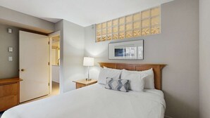 Ein Hotelzimmer mit Bett, Nachttisch, Lampe, Tür und Fenster mit Blick.