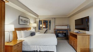 Een hotelkamer met een bed, nachtkastje, lamp, televisie, open haard en een raam met gordijnen.