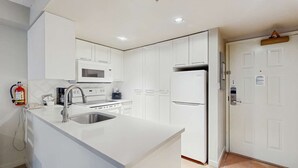 A modern kitchen with white cabinetry, a stainless steel sink, a microwave, and a refrigerator. - Whistler - Whistler Peak Lodge 214 (Whistler)