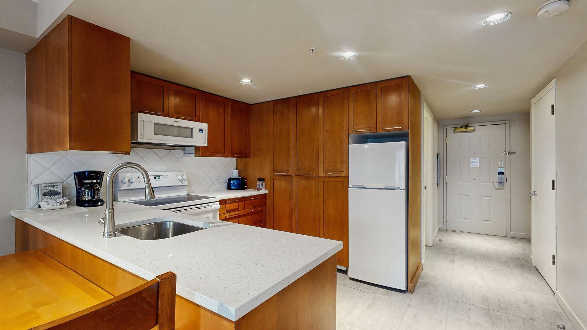 A compact kitchen with wooden cabinets, a microwave, a refrigerator, a sink, and a coffee maker.
