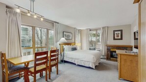 Een hotelkamer met een bed, een bureau met stoelen, een open haard en grote ramen.