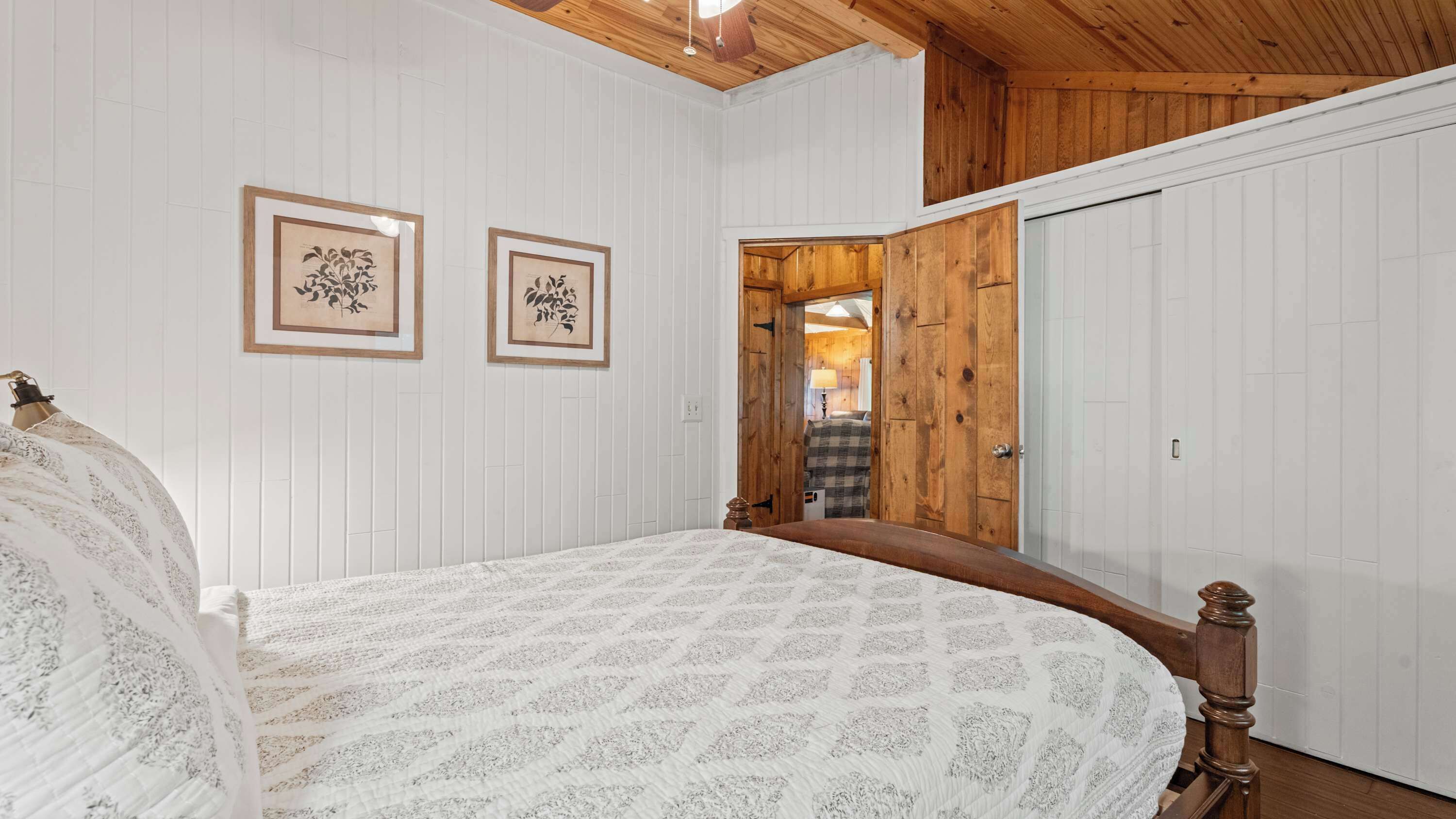 Une chambre à coucher avec un lit, deux tableaux encadrés au mur, une porte en bois et un plafond avec des poutres en bois.