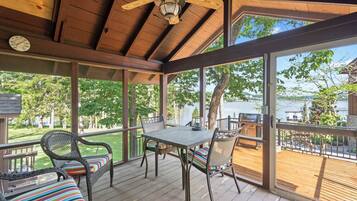 A covered outdoor deck with a table and chairs, overlooking a body of water.