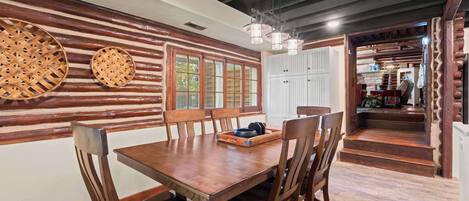 A dining area with a wooden table and chairs, a window with blinds, and a hanging light fixture.