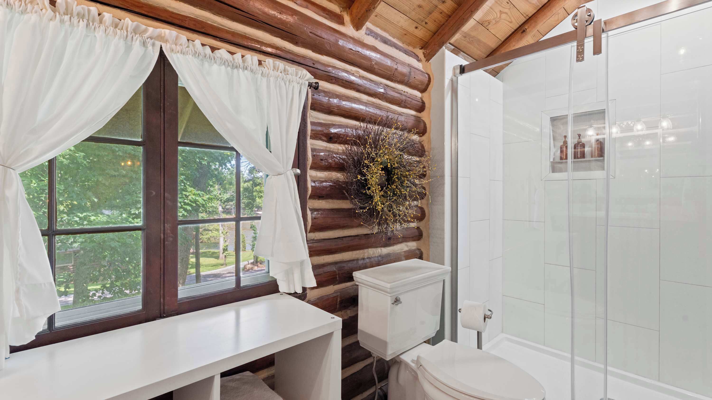 A bathroom with a wooden log wall, a toilet, a sink, and a shower.