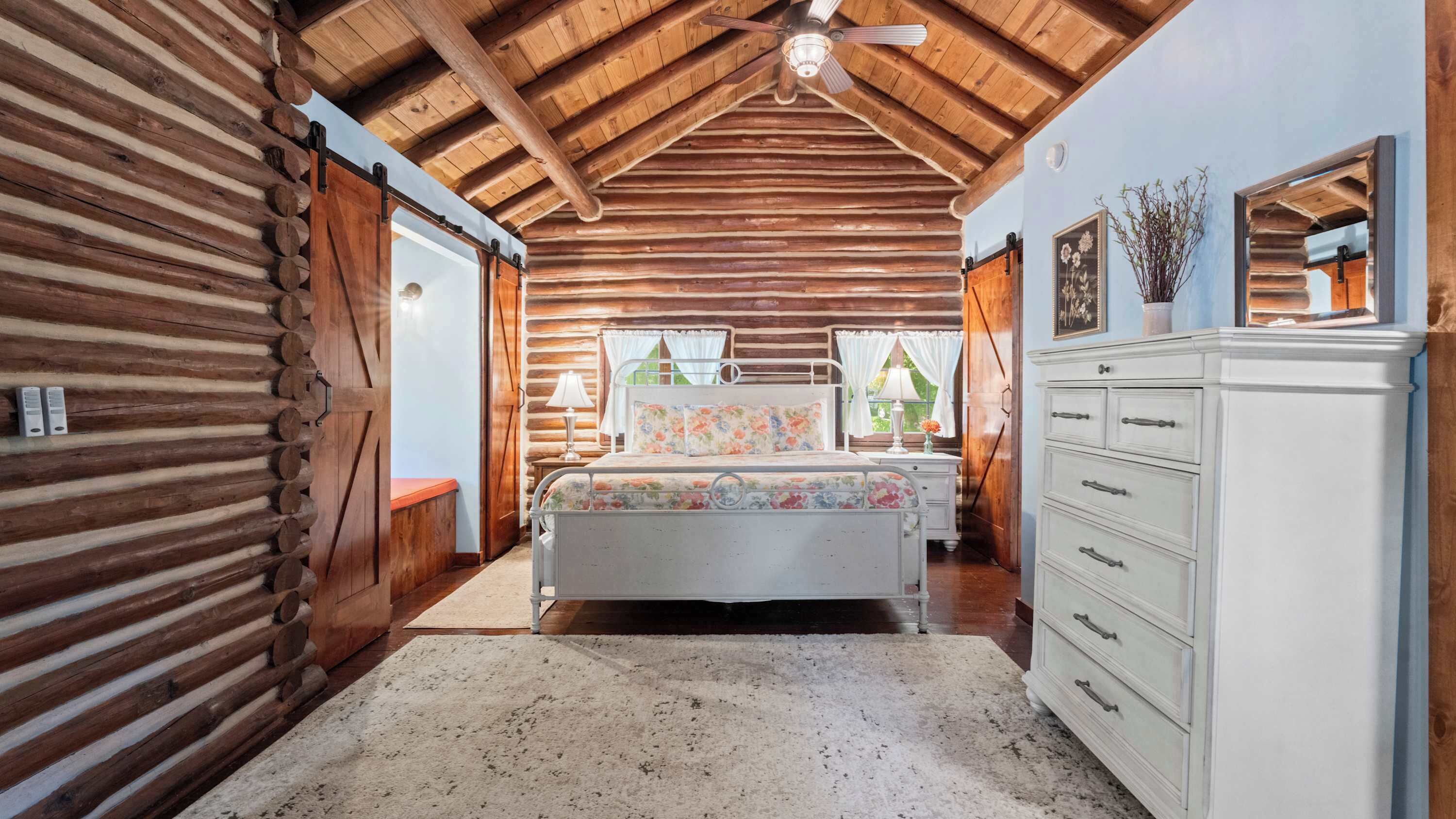 A log cabin interior with a bed, dresser, and a ceiling fan.