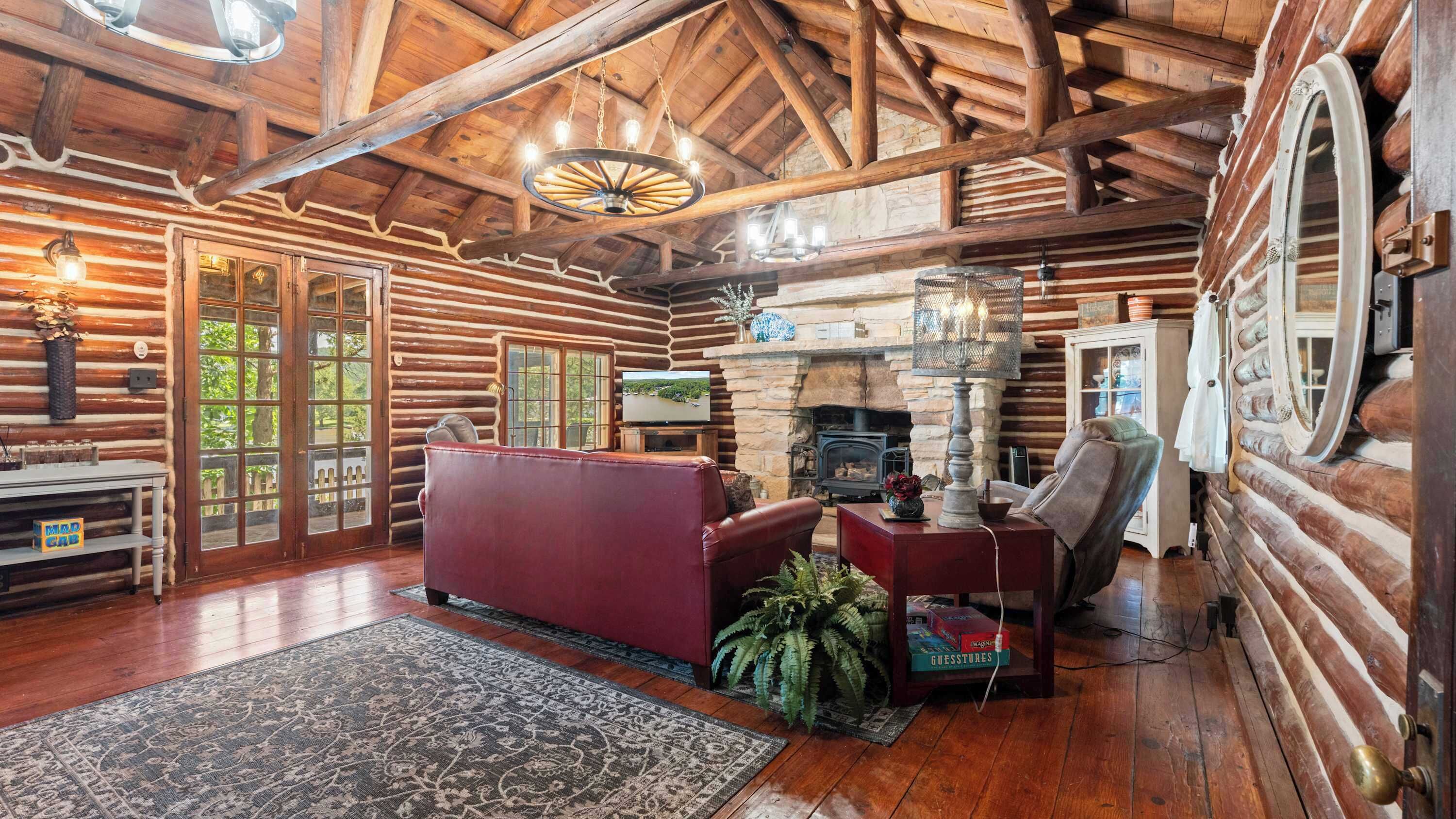 A log cabin interior with a fireplace, leather sofa, and a television.
